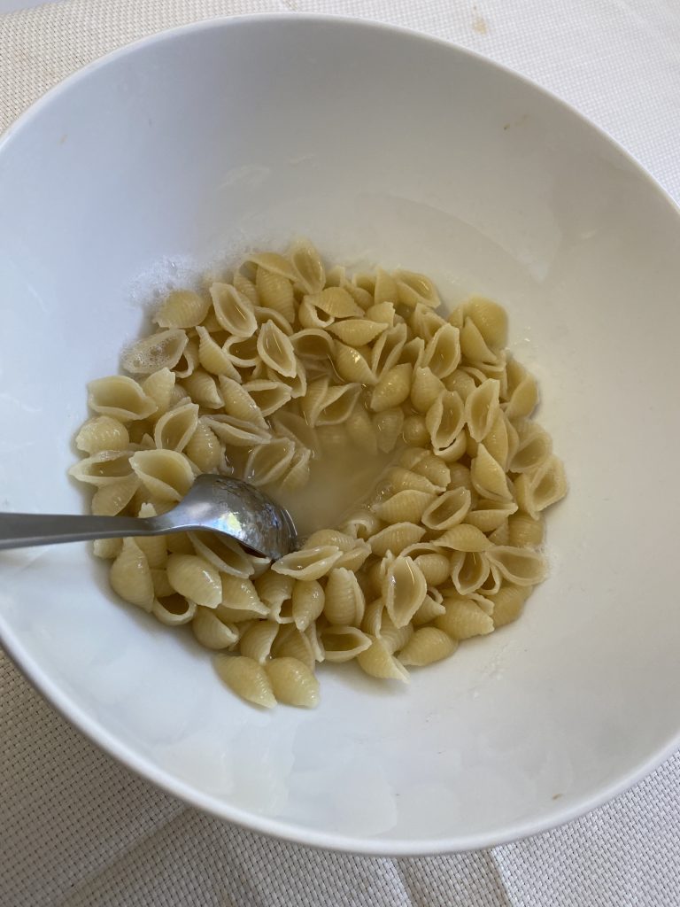 A white bowl filled with pasta noodles and starchy water bring stirred by a stainless steel spoon